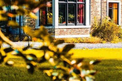 Bâtiment moderne en bois noir avec toit en pente, entouré d'arbres et d'un sol couvert de feuilles d'automne.