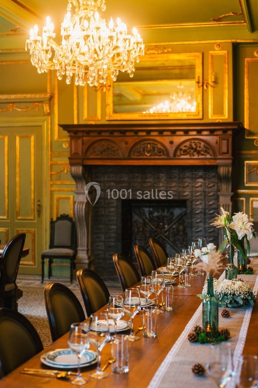 Table élégamment dressée dans une salle ornée de boiseries, avec un lustre et une cheminée décorative en arrière-plan.