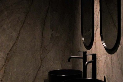 Bâtiment moderne en bois noir avec toit en pente, entouré d'arbres et d'un sol couvert de feuilles d'automne.