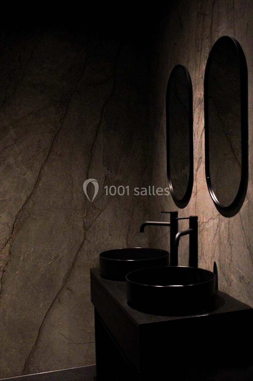 Deux lavabos noirs avec robinets assortis, surmontés de miroirs ovales, dans une salle de bain sombre aux murs en pierre.