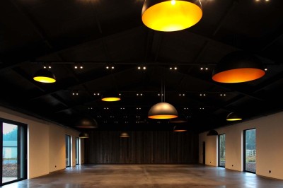 Bâtiment moderne en bois noir avec toit en pente, entouré d'arbres et d'un sol couvert de feuilles d'automne.