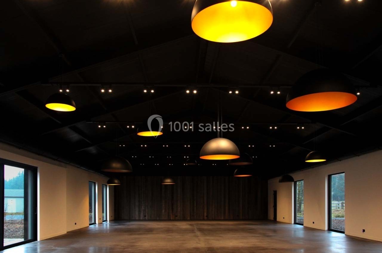 Salle vide avec un plafond sombre, éclairée par des suspensions lumineuses jaunes et des fenêtres latérales.