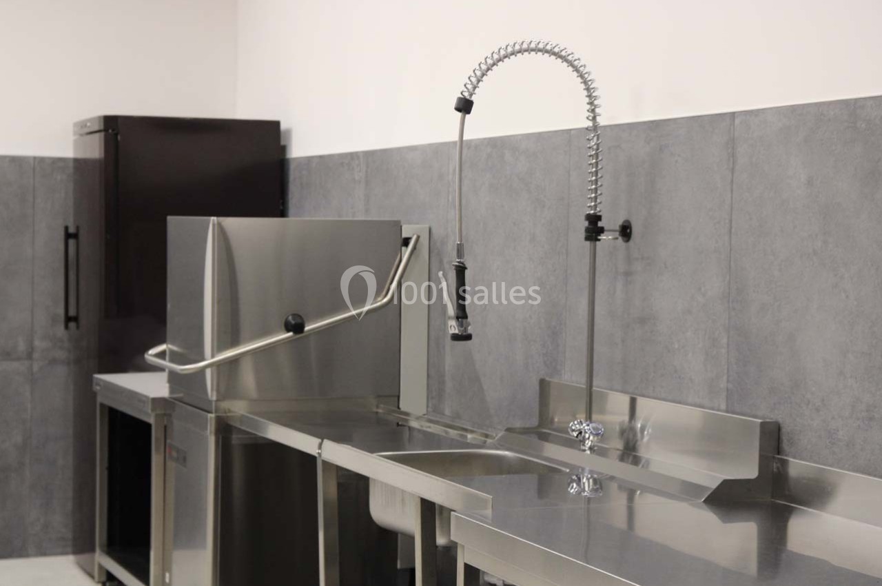 Évier en acier inoxydable avec robinet flexible, à côté d'un lave-vaisselle professionnel et d'un réfrigérateur.