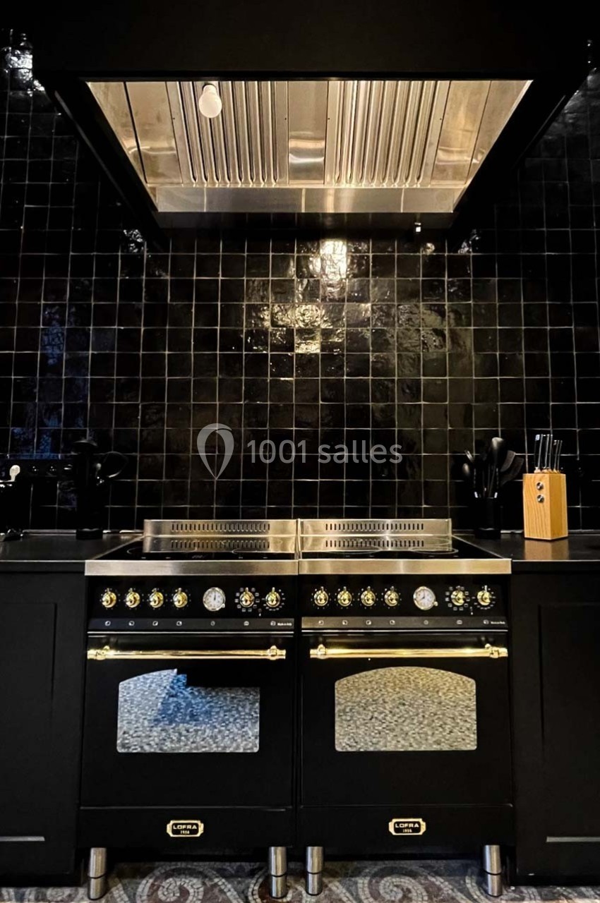 Cuisinière noire et dorée avec hotte en acier inoxydable, entourée de carreaux muraux noirs brillants.