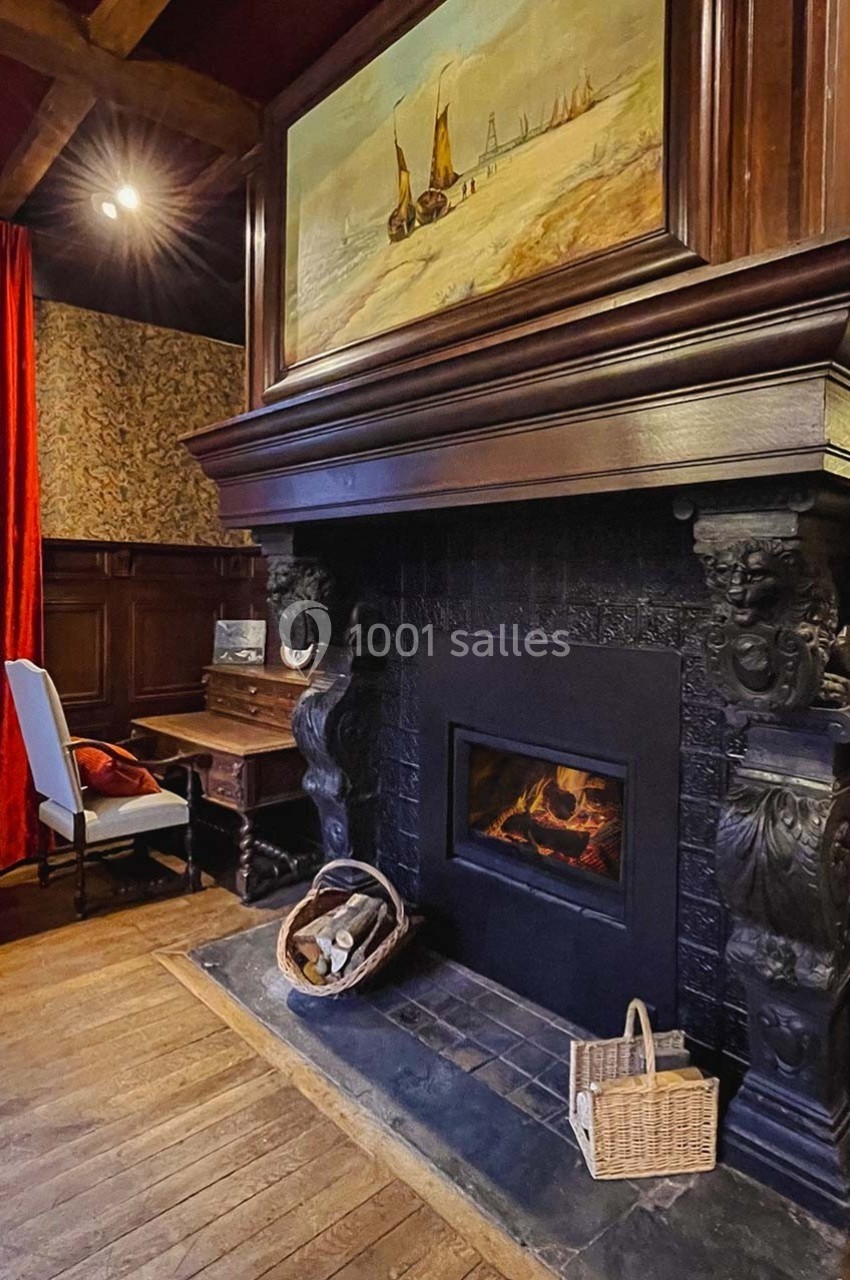 Cheminée en pierre sculptée avec feu allumé, entourée de meubles en bois sombre et rideaux rouges dans une pièce chaleureuse.