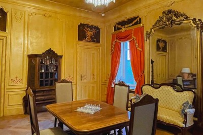 Bâtiment moderne en bois noir avec toit en pente, entouré d'arbres et d'un sol couvert de feuilles d'automne.