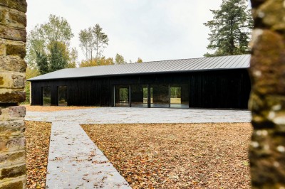 Bâtiment moderne en bois noir avec toit en pente, entouré d'arbres et d'un sol couvert de feuilles d'automne.
