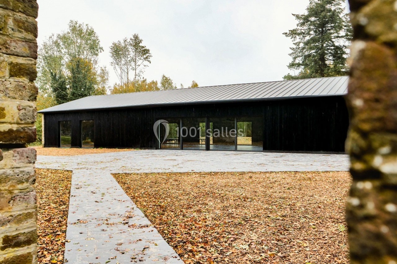 Bâtiment moderne en bois noir avec toit en pente, entouré d'arbres et d'un sol couvert de feuilles d'automne.