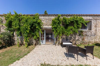 Vieille brouette en bois devant un mur en pierre et une porte en bois usée, sous un ciel dégagé.