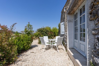 Vieille brouette en bois devant un mur en pierre et une porte en bois usée, sous un ciel dégagé.