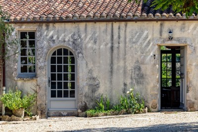 Vieille brouette en bois devant un mur en pierre et une porte en bois usée, sous un ciel dégagé.