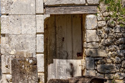 Vieille brouette en bois devant un mur en pierre et une porte en bois usée, sous un ciel dégagé.