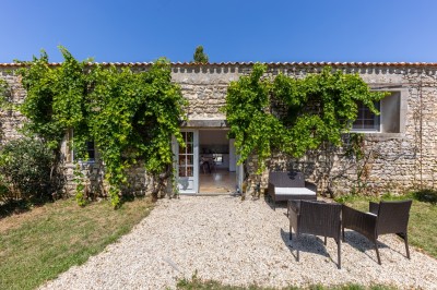 Vieille brouette en bois devant un mur en pierre et une porte en bois usée, sous un ciel dégagé.