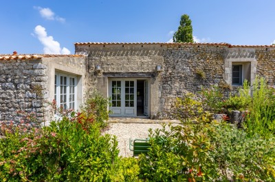 Vieille brouette en bois devant un mur en pierre et une porte en bois usée, sous un ciel dégagé.