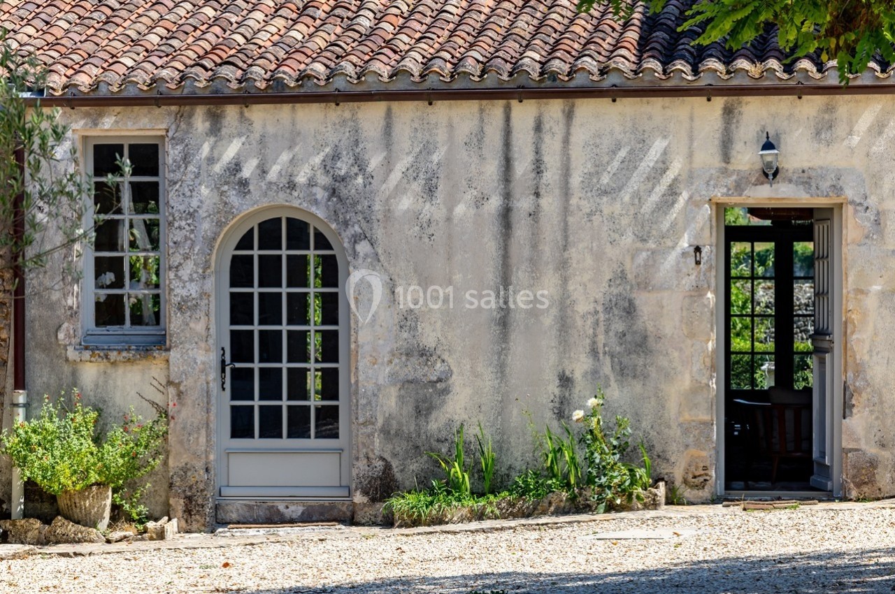 Façade d'une maison en pierre avec portes vitrées, fenêtres et plantes devant un sol en gravier.