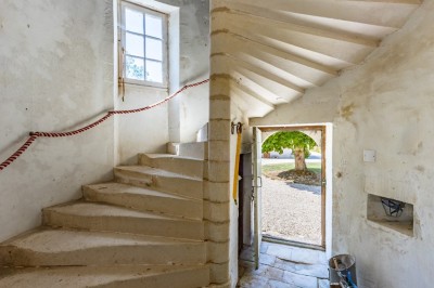 Vieille brouette en bois devant un mur en pierre et une porte en bois usée, sous un ciel dégagé.