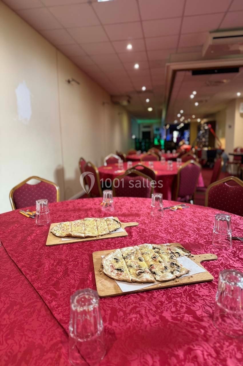 Des tables rouges dressées avec des verres et des planches de pizzas dans une salle de réception éclairée.