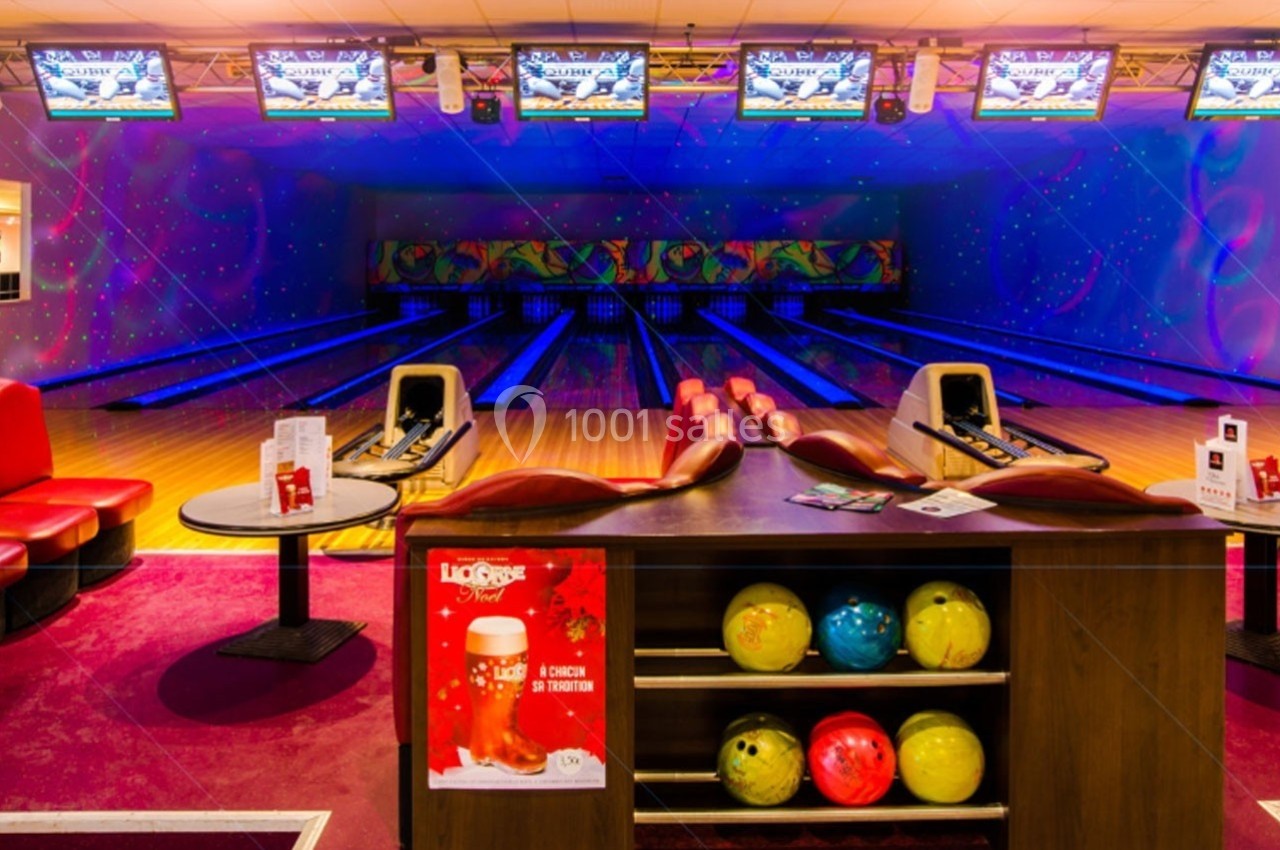 Salle de bowling colorée avec plusieurs pistes, écran au fond et comptoir contenant des boules de bowling.