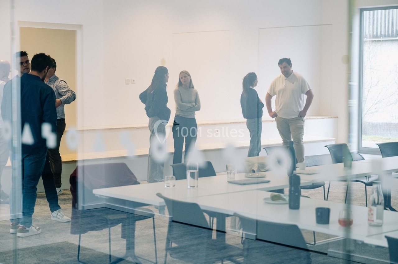 Des personnes discutent debout dans une salle de réunion lumineuse avec des tables et des chaises en avant-plan.