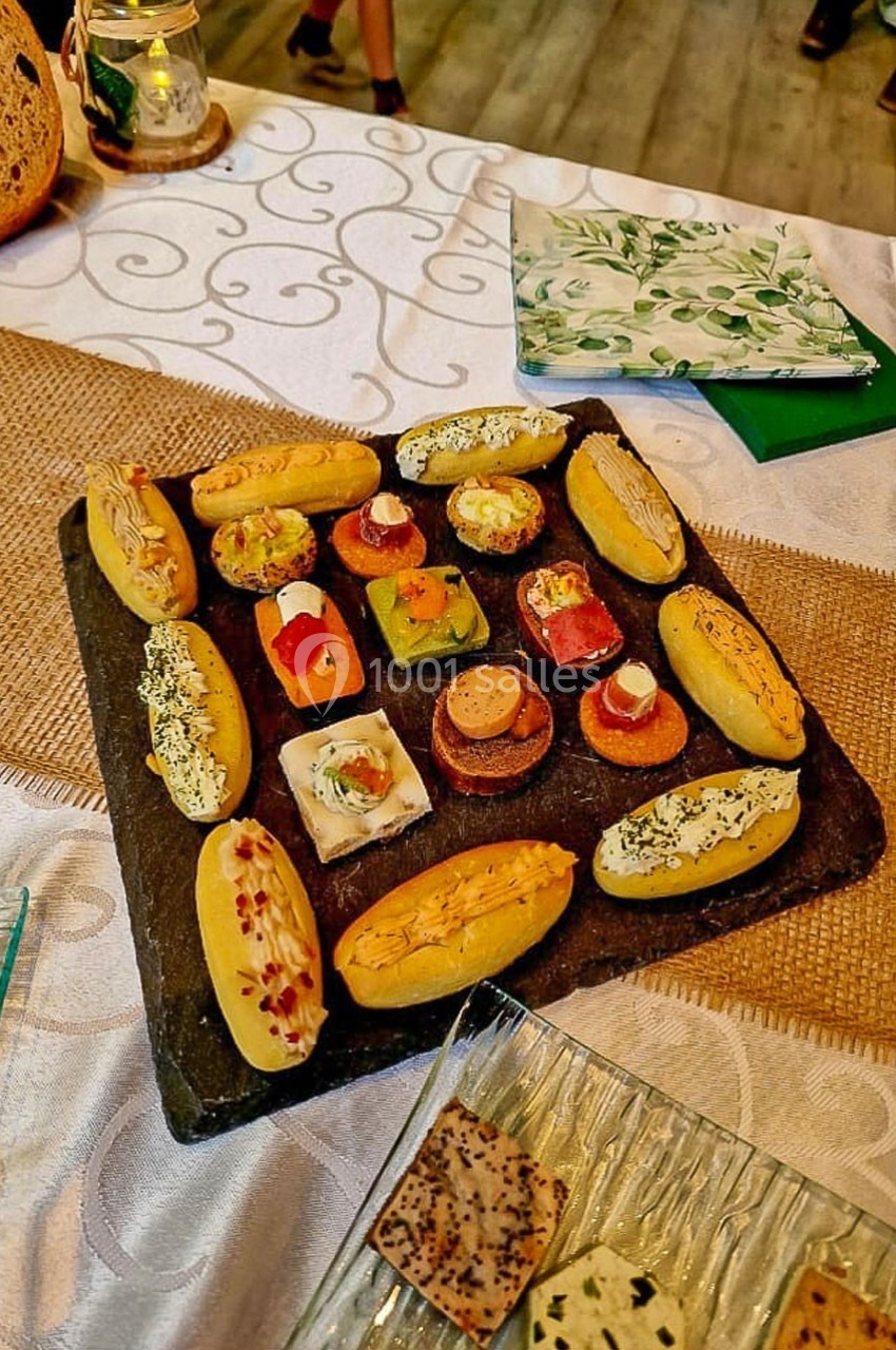 Plateau de canapés variés disposés sur une ardoise, accompagné de pain et de serviettes décoratives sur une table dressée.