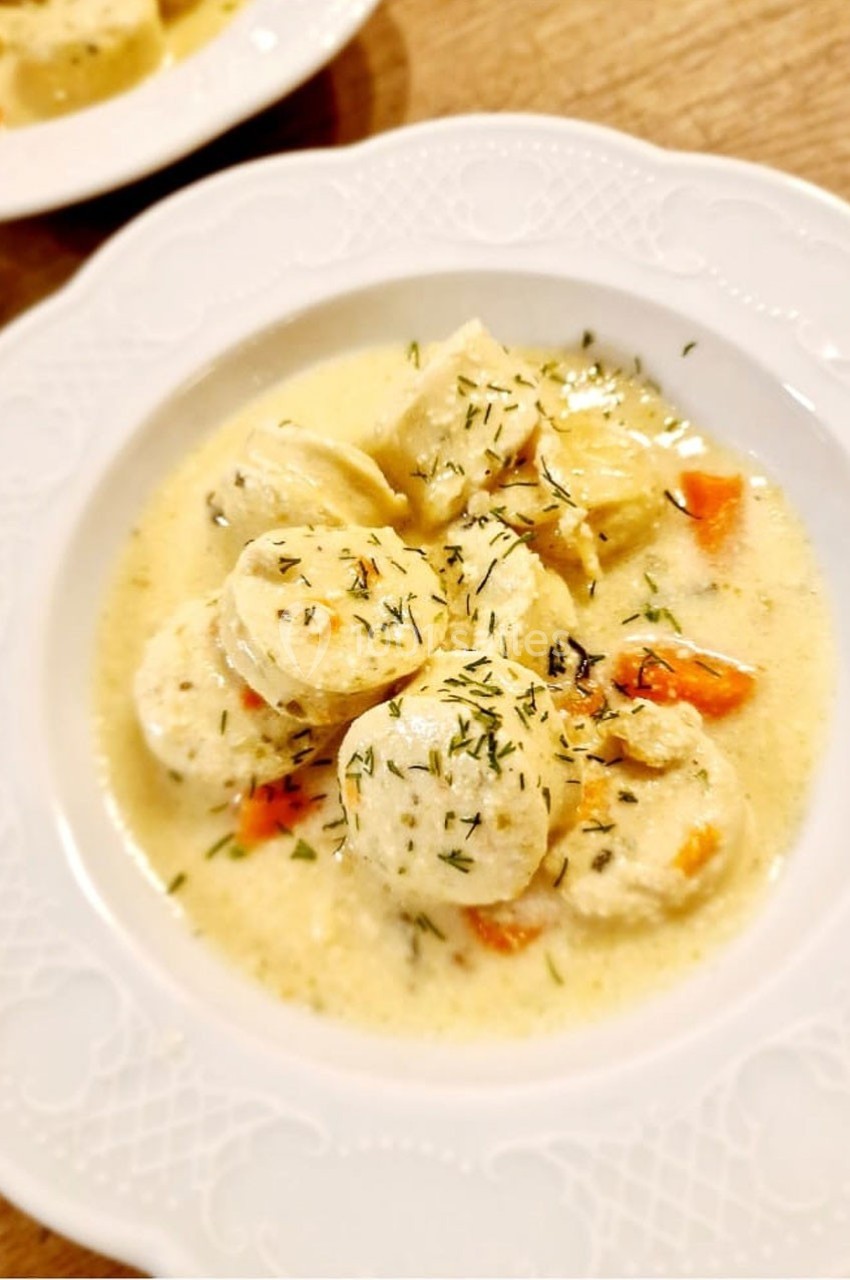 Assiette de quenelles nappées de sauce crémeuse, garnies de carottes et d'herbes, servie sur une table en bois.