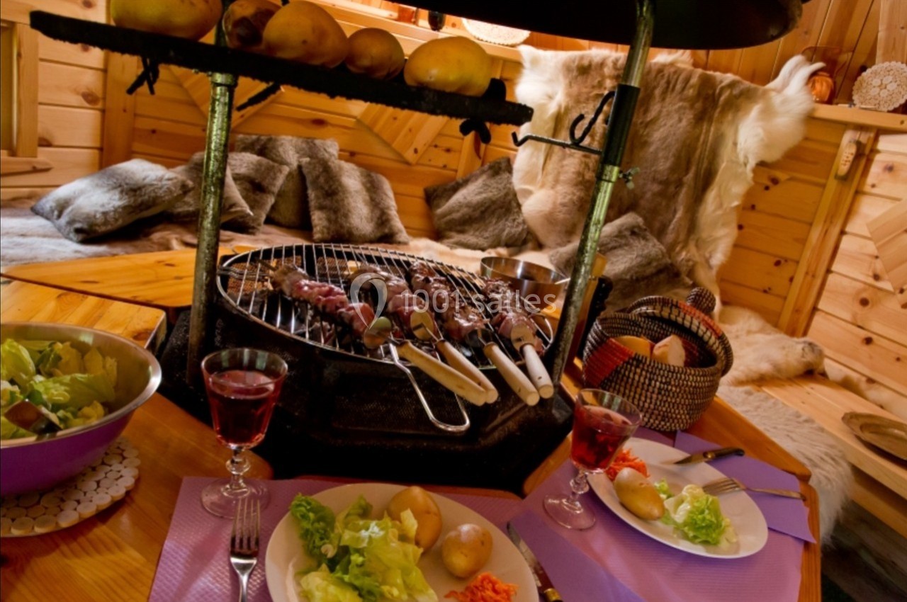 Brochettes grillées sur un barbecue intérieur entouré de plats de légumes et de boissons dans un chalet en bois.