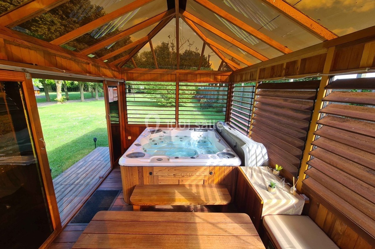 Abri en bois avec un jacuzzi intégré, entouré de baies vitrées et ouvert sur un jardin verdoyant.