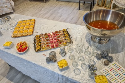 Groupe de personnes réunies dans une salle lumineuse autour d'un buffet varié avec boissons et plats.