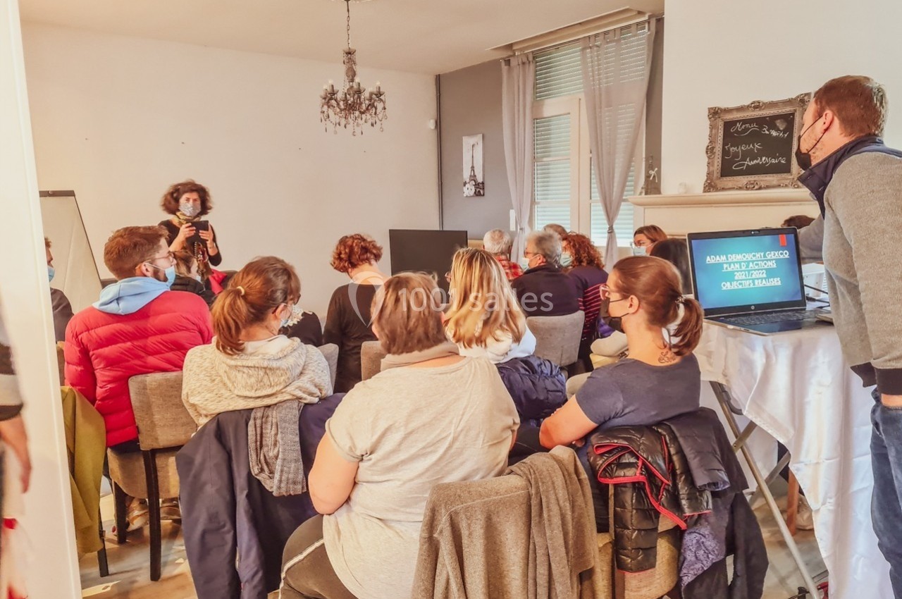 Un groupe de personnes assises dans une salle, écoutant une présentation donnée par une intervenante debout.
