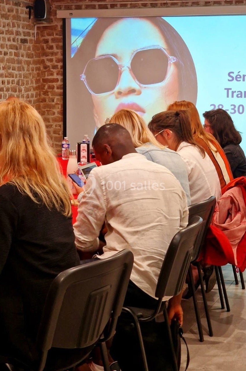 Des personnes assises dans une salle de conférence, regardant un écran affichant une image et des informations.