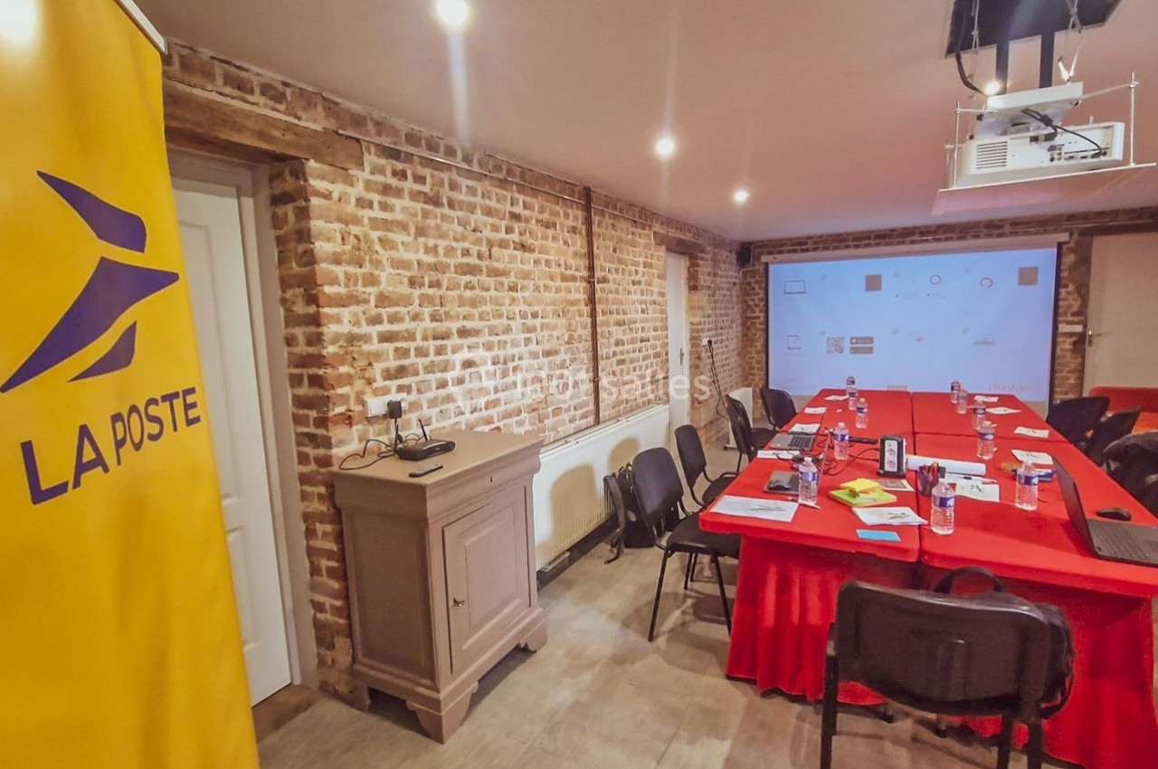 Salle de réunion avec table rouge, chaises noires, matériel de présentation et un panneau ’La Poste’ visible à gauche.