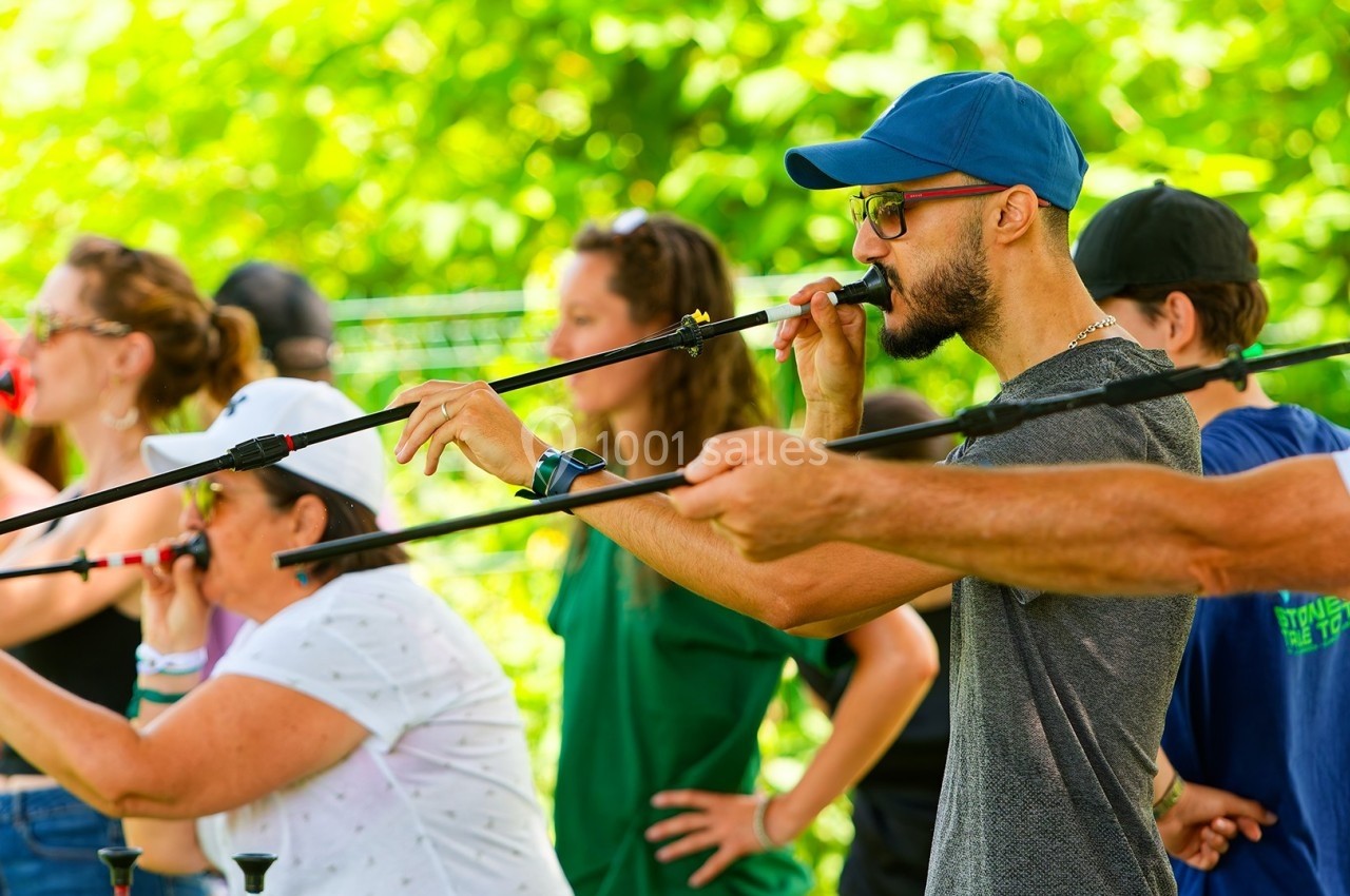 Des personnes participent à une activité de tir à la sarbacane en plein air, entourées de verdure.