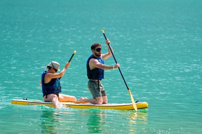Voilier blanc amarré sur un lac calme, entouré de montagnes verdoyantes sous un ciel dégagé.