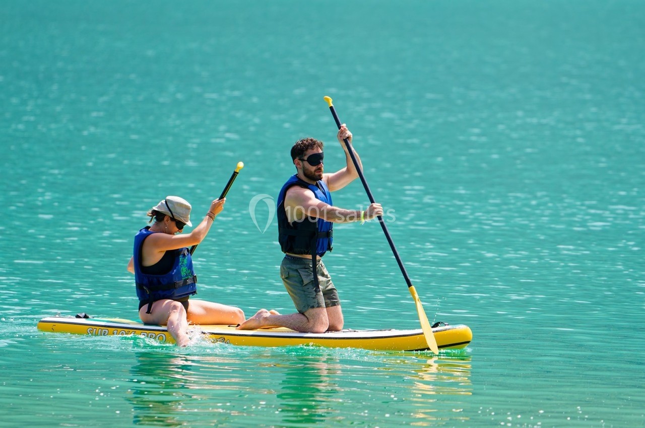 Deux personnes en gilets de sauvetage pagaient sur un paddle gonflable dans une eau turquoise calme.