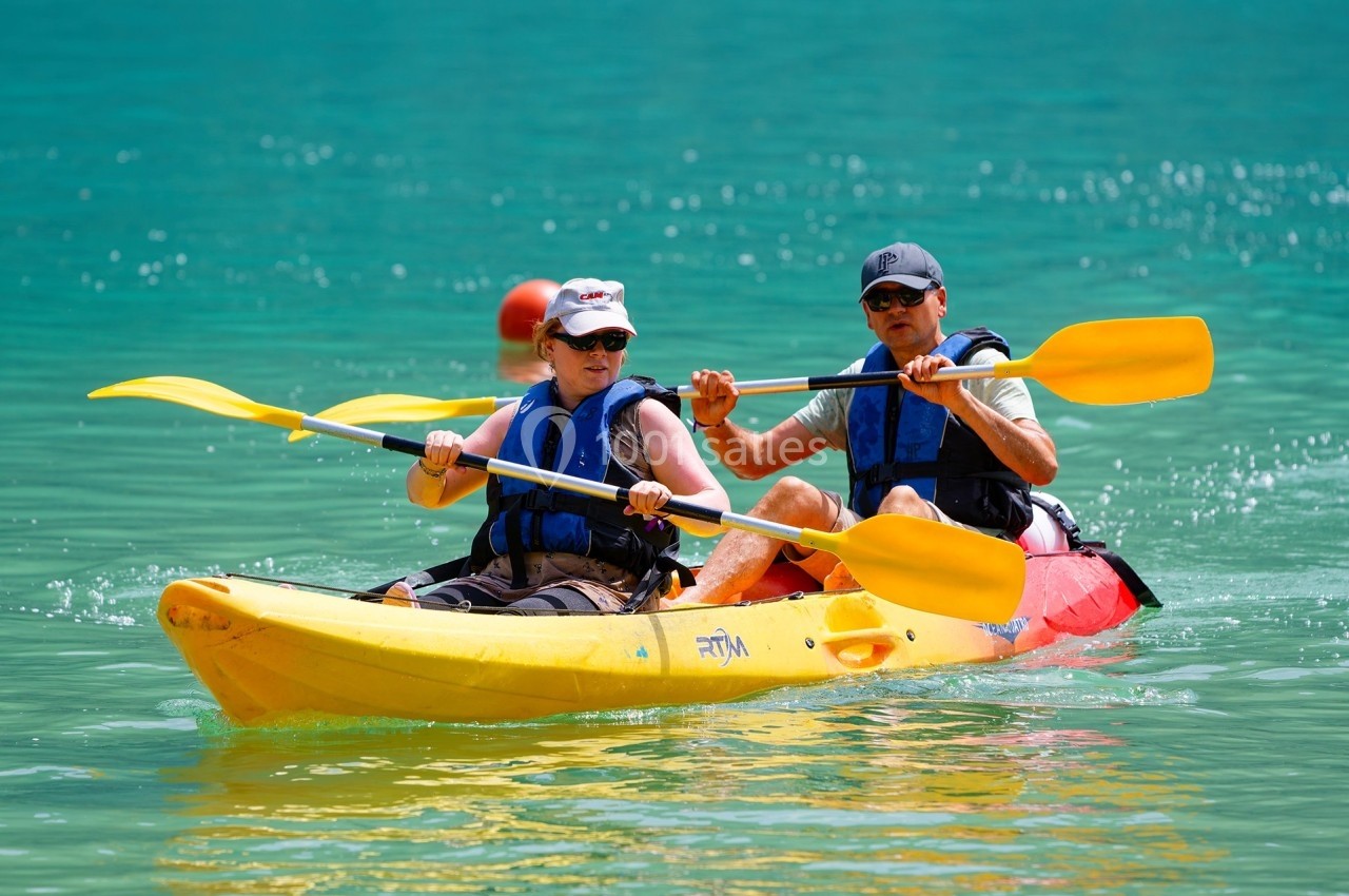 Deux personnes pagayant ensemble dans un kayak jaune sur une eau turquoise par temps ensoleillé.