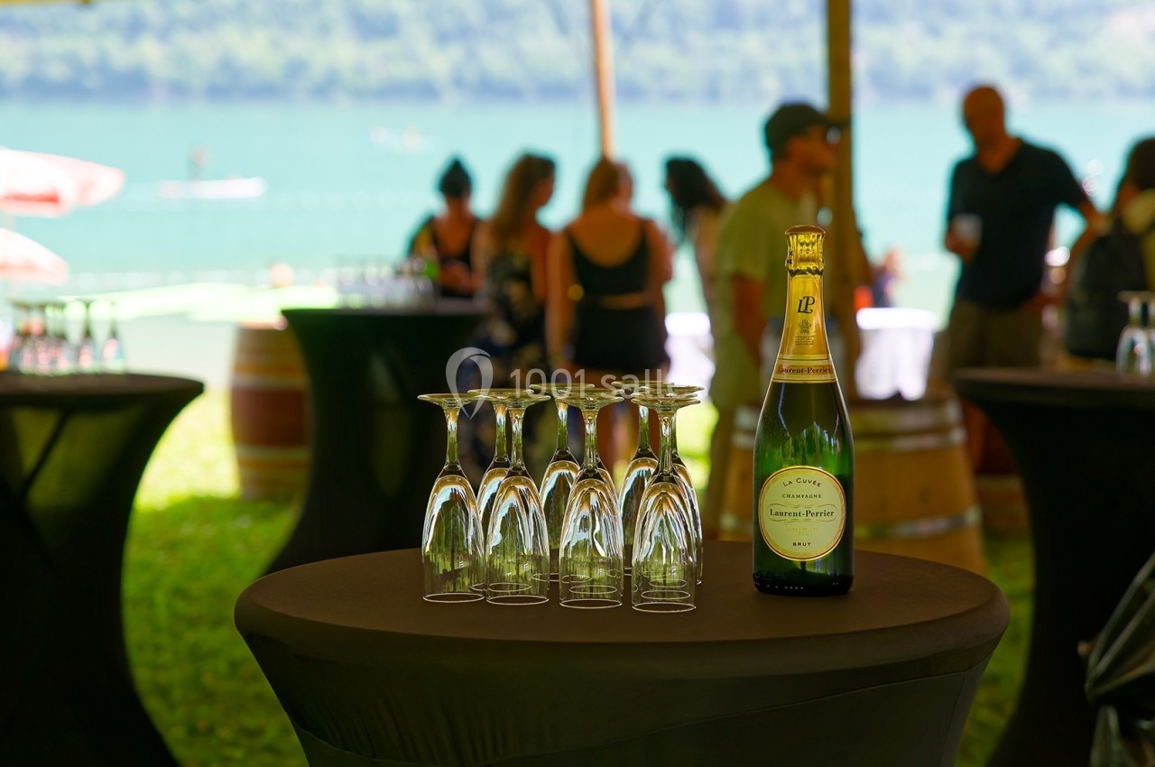 Bouteille de champagne et verres retournés sur une table lors d'un événement en extérieur près d'un lac.