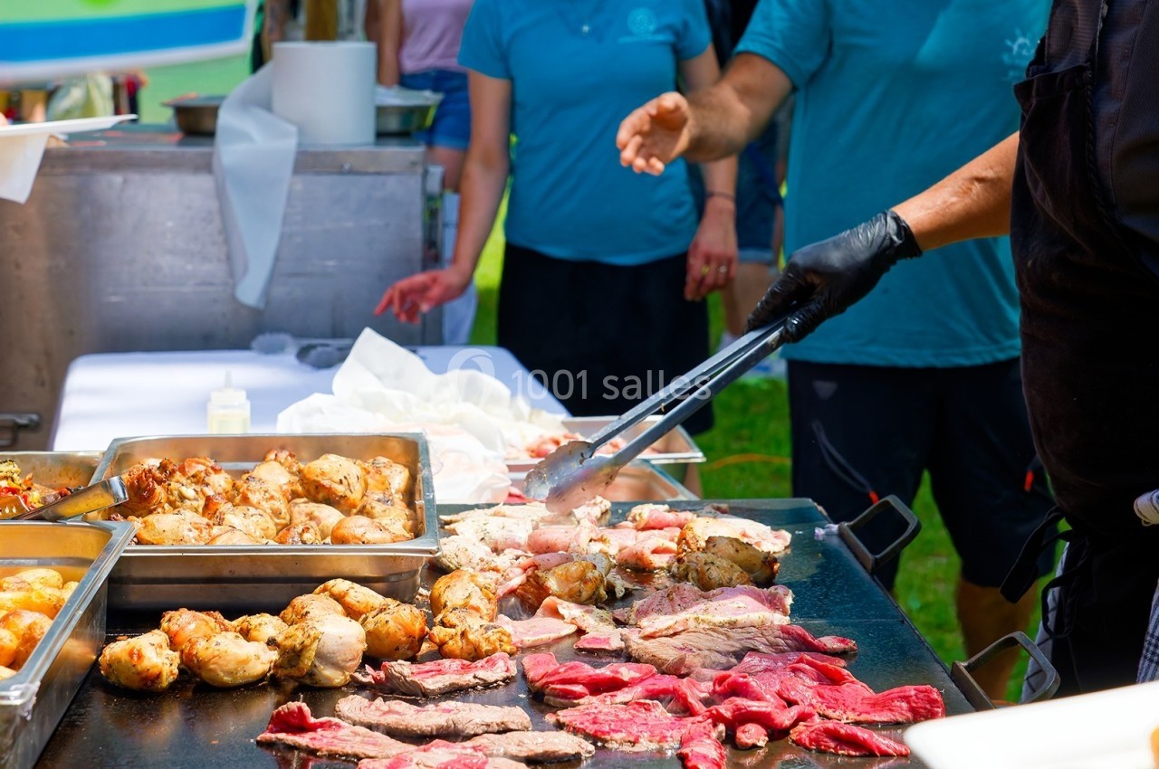 Personne préparant de la viande grillée sur une plaque chauffante lors d'un événement en plein air.