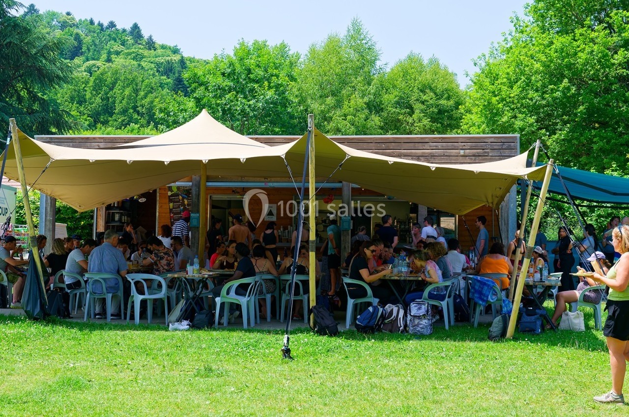 Un groupe de personnes assises et debout sous une grande tente beige dans un espace vert en plein air.