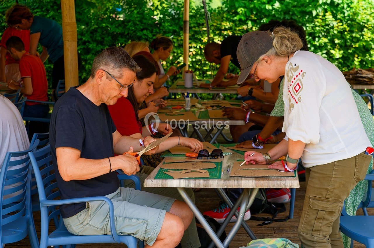 Des personnes participent à un atelier créatif en plein air, découpant et assemblant des matériaux sur des tables.