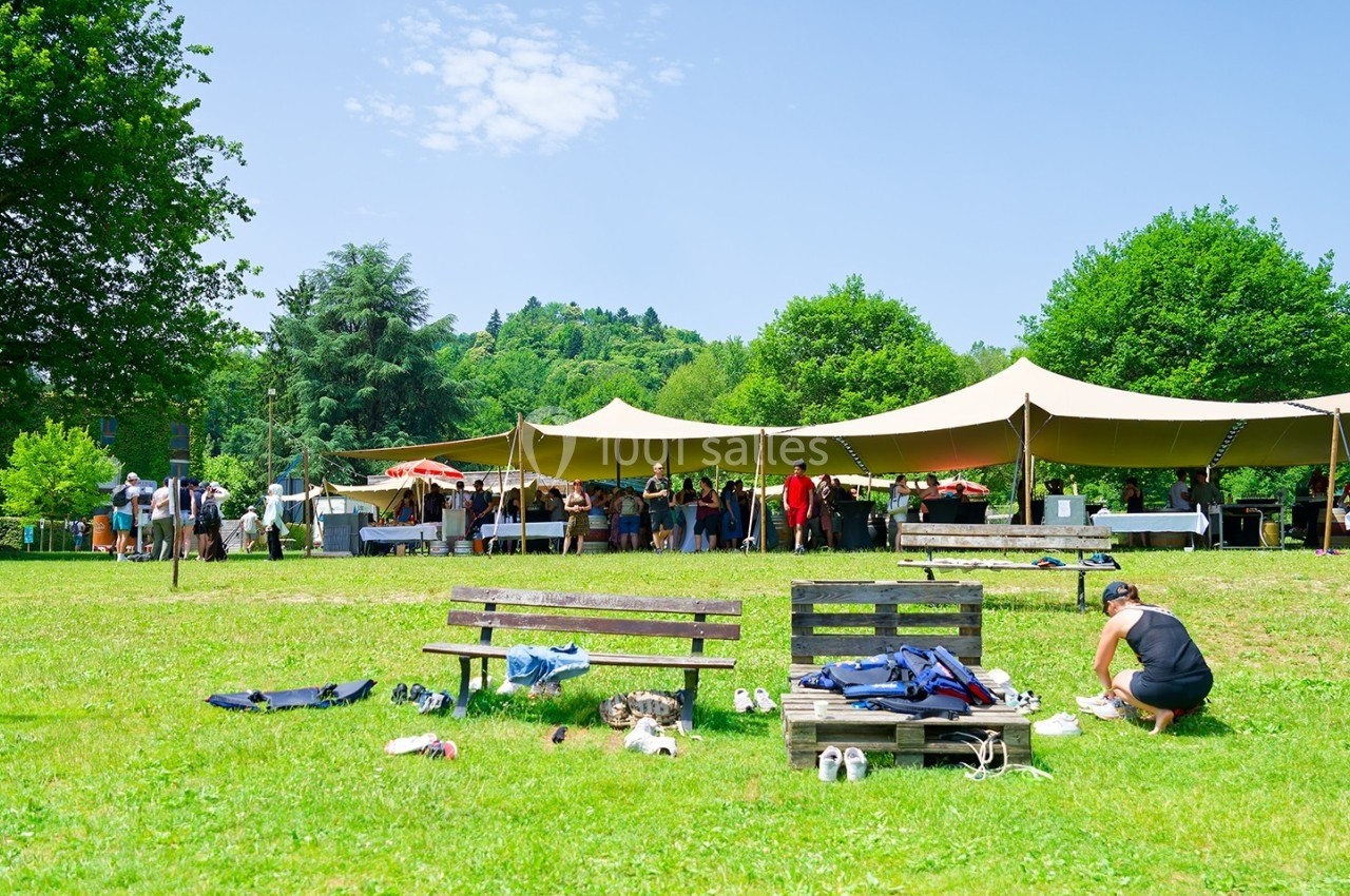 Des personnes rassemblées sous des tentes dans un parc verdoyant, avec des bancs et des vêtements posés au sol.