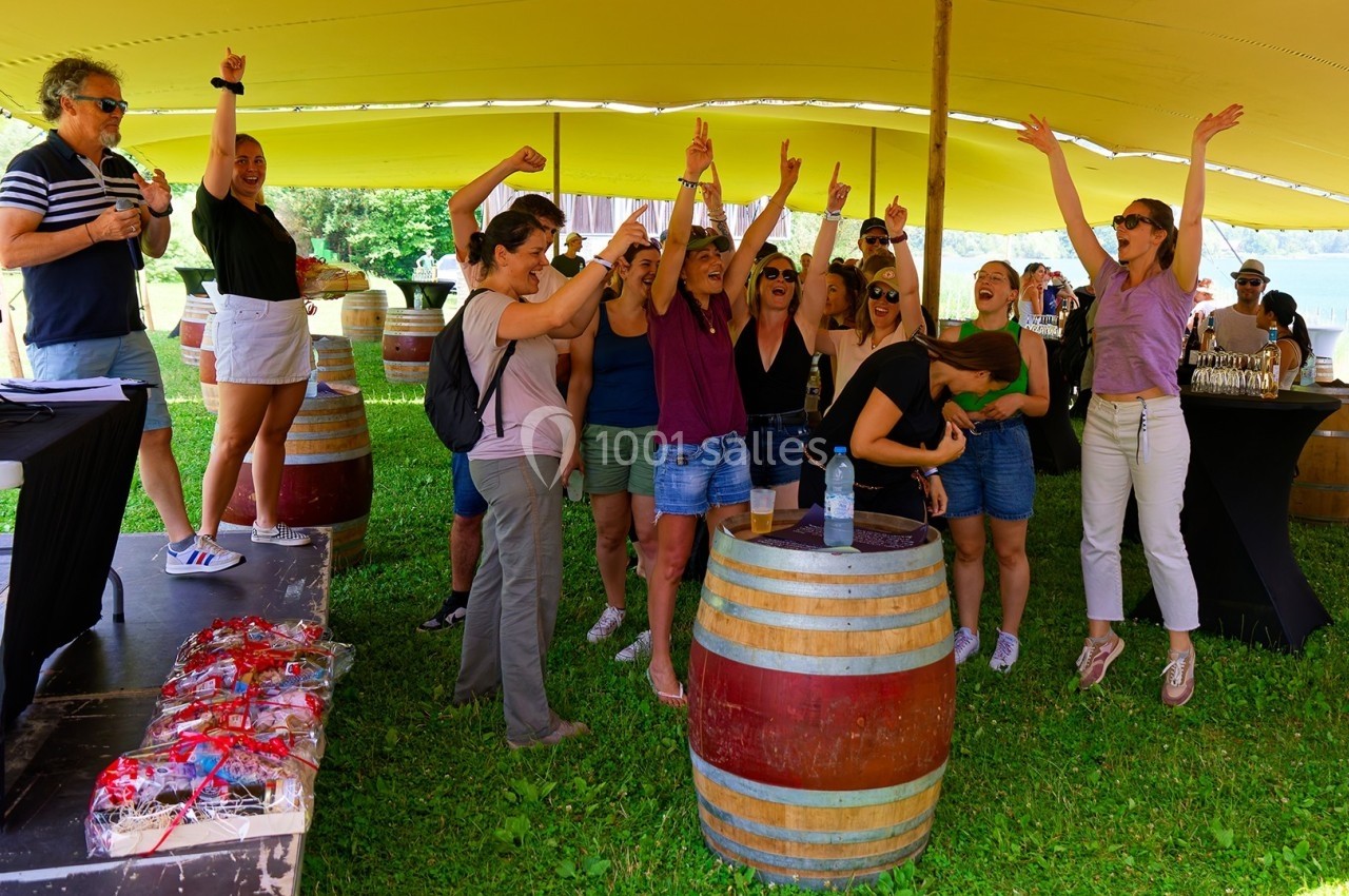 Un groupe de personnes enthousiastes célèbre sous une tente, entouré de tonneaux et d'éléments festifs en extérieur.