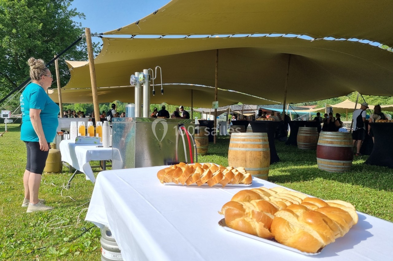 Tables dressées en extérieur avec des pains, des tonneaux en arrière-plan et des invités sous une tente.