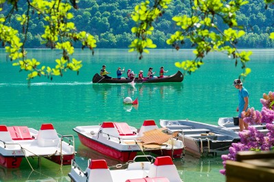 Voilier blanc amarré sur un lac calme, entouré de montagnes verdoyantes sous un ciel dégagé.