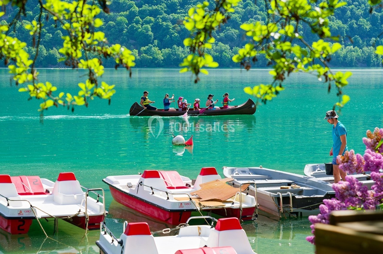 Des pédalos amarrés au bord d'un lac turquoise, avec un groupe en canoë au loin entouré de végétation.