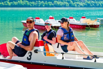 Voilier blanc amarré sur un lac calme, entouré de montagnes verdoyantes sous un ciel dégagé.