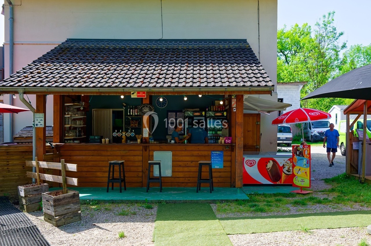 Kiosque en bois avec comptoir, entouré de parasols et de chaises, situé dans un espace extérieur ensoleillé.