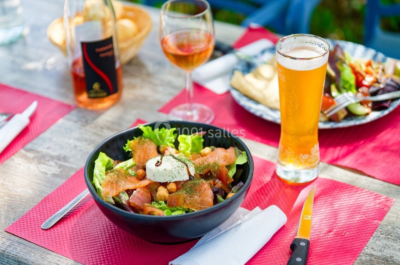 Salade composée avec saumon fumé, fromage frais, croûtons et légumes, servie sur une table avec boissons et couverts.