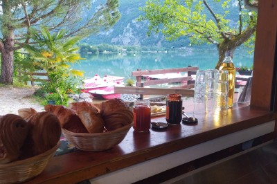 Voilier blanc amarré sur un lac calme, entouré de montagnes verdoyantes sous un ciel dégagé.