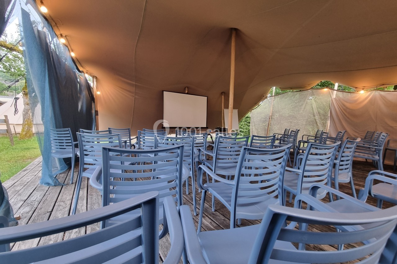 Chaises bleues disposées devant un écran de projection sous une tente beige, en extérieur.