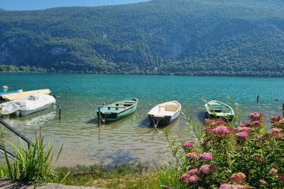 Voilier blanc amarré sur un lac calme, entouré de montagnes verdoyantes sous un ciel dégagé.